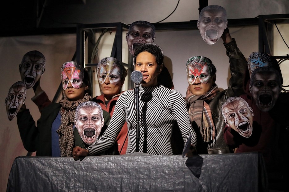 Actor Sara Zwangobani, surrounded by masked cast members, as Marc Antony in Julius Caesar.