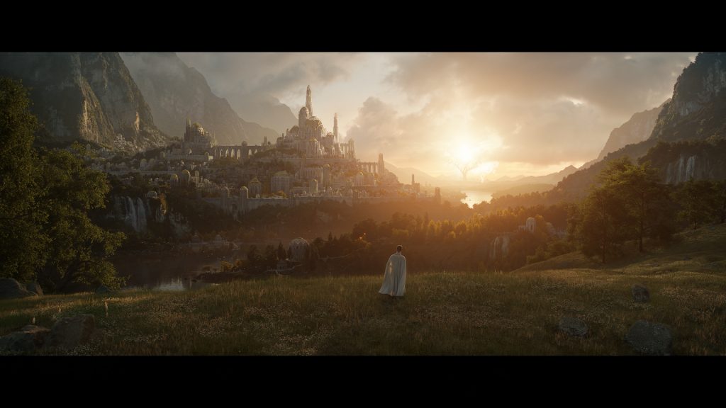 The first official image from Amazon's Lord of the Rings series. It shows a figure, perhaps an elf, cloaked in white, gazing towards a distant city. In the further distance we see the Two Trees, ablaze with light. Between the city and the trees there is an area of water.