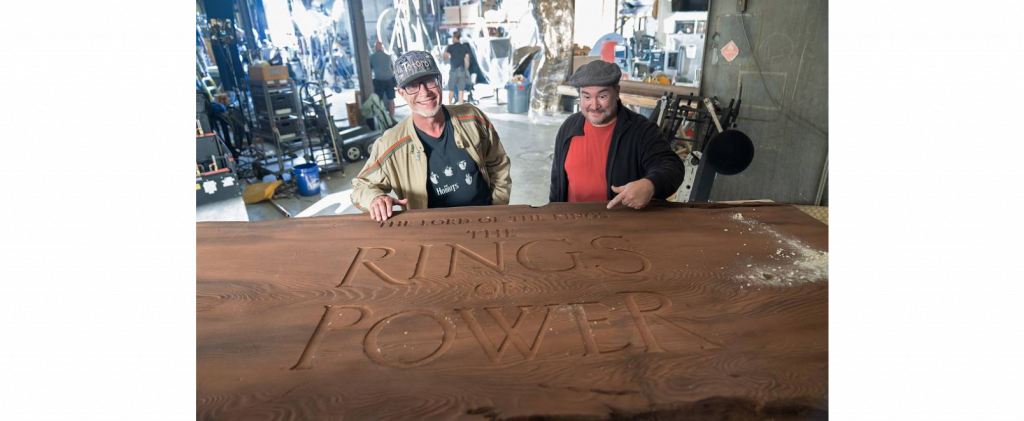Staffers Quickbeam and Justin stand behind the carved redwood piece, showed the title of the upcoming Prime Video show