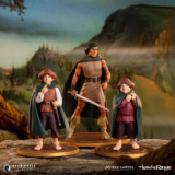 Aragorn with sword flanked by two Hobbit figures in cloaks on a rocky display against a fantasy landscape backdrop.