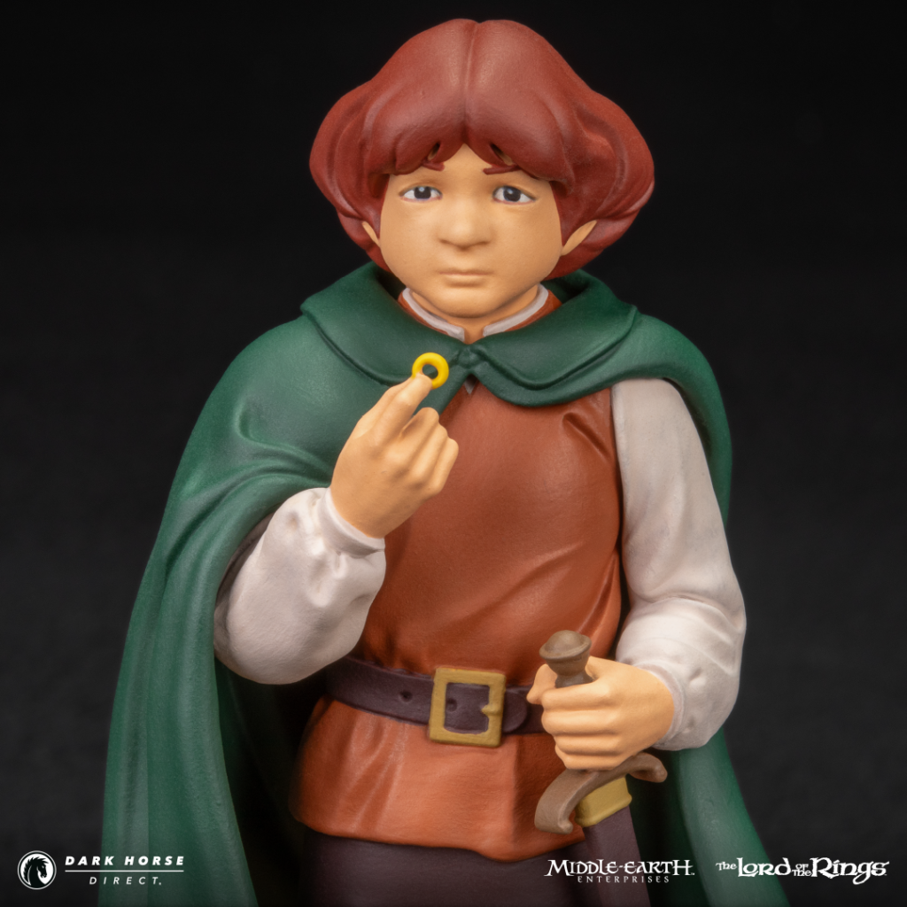 Hobbit action figure in a green cape and orange tunic, holding a gold ring with a small sword at his belt.