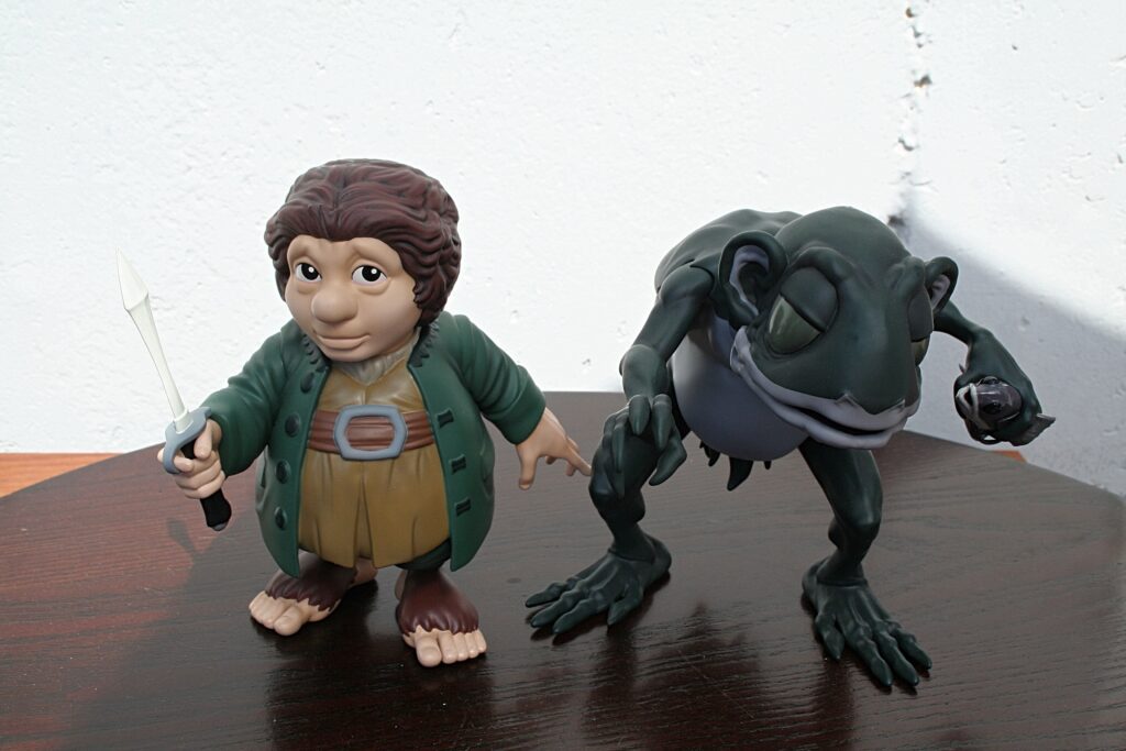 Hobbit-like action figure with a sword beside a gray dragon on a dark wooden table