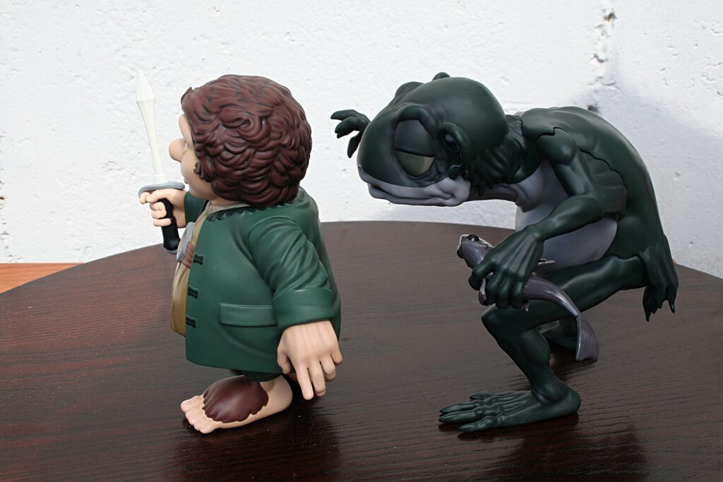 Action figure of a man in a green coat holding a sword, with a dark dragon looming behind him on a wooden table surface.