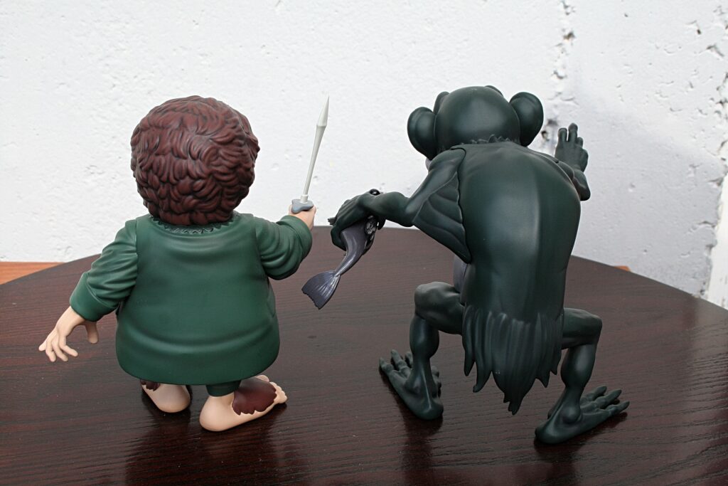 Back view of two toy figurines on a table: a boy with a sword facing a dark creature in a confrontational pose.