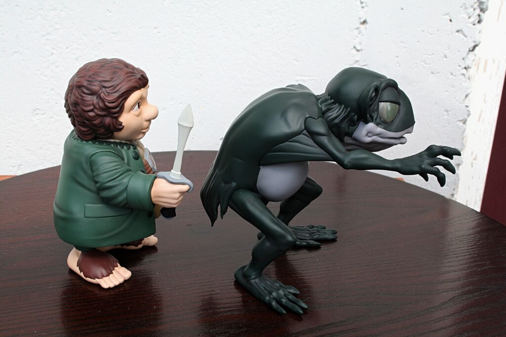 Cartoon figurine of a man in a green coat holding a knife, facing a crouched dark creature on a wooden table.
