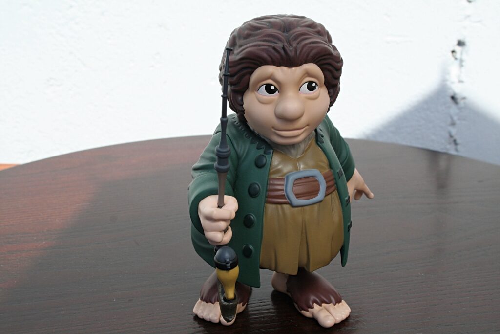 Indiana Jones-style action figure holding a whip, wearing a green jacket and brown outfit, standing on a wooden table.