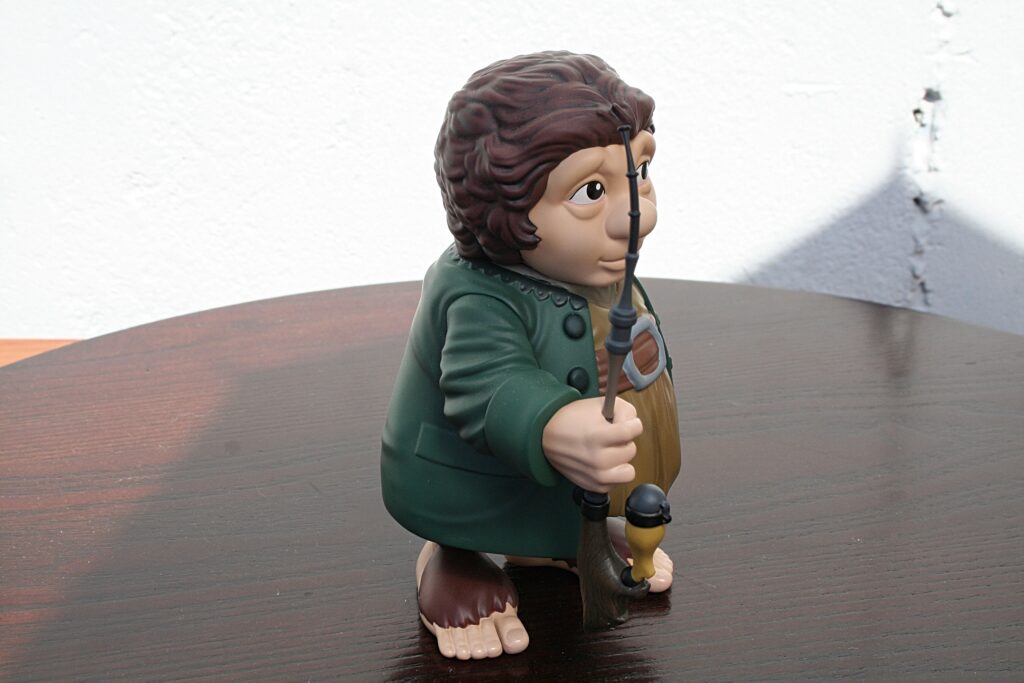 Plastic figurine of a Hobbit-like man with brown hair in a green cloak, kneeling on a wooden table and holding a staff.