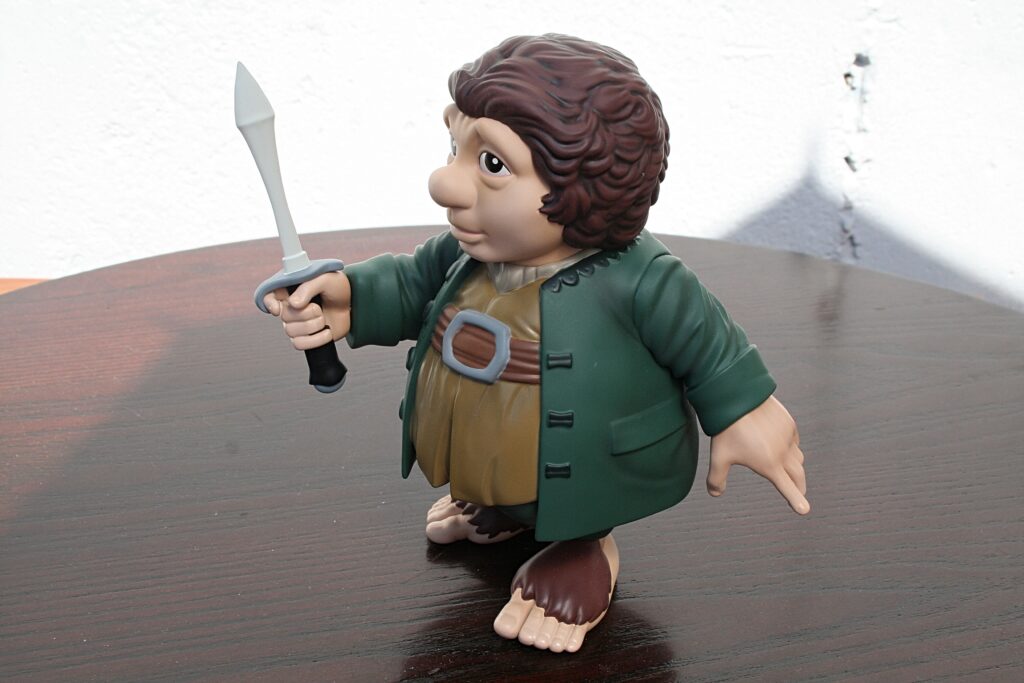 Hobbit-style action figure in a green coat raises a dagger in a ready pose on a wooden table.