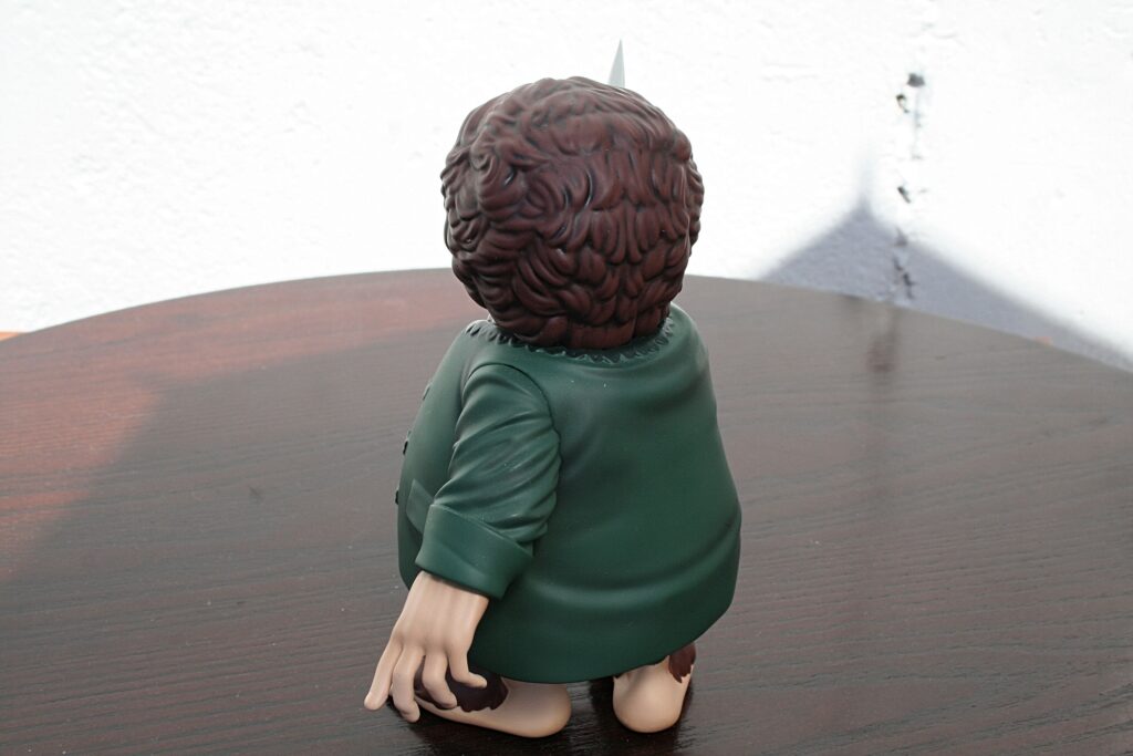 Plastic figurine of a person with a brown brain-shaped head in a green dress, seen from behind on a wooden table surface.