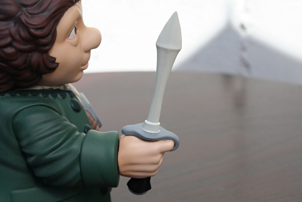 Toy knight action figure gripping a gray spear with both hands, shown in a green tunic and brown hair, facing left