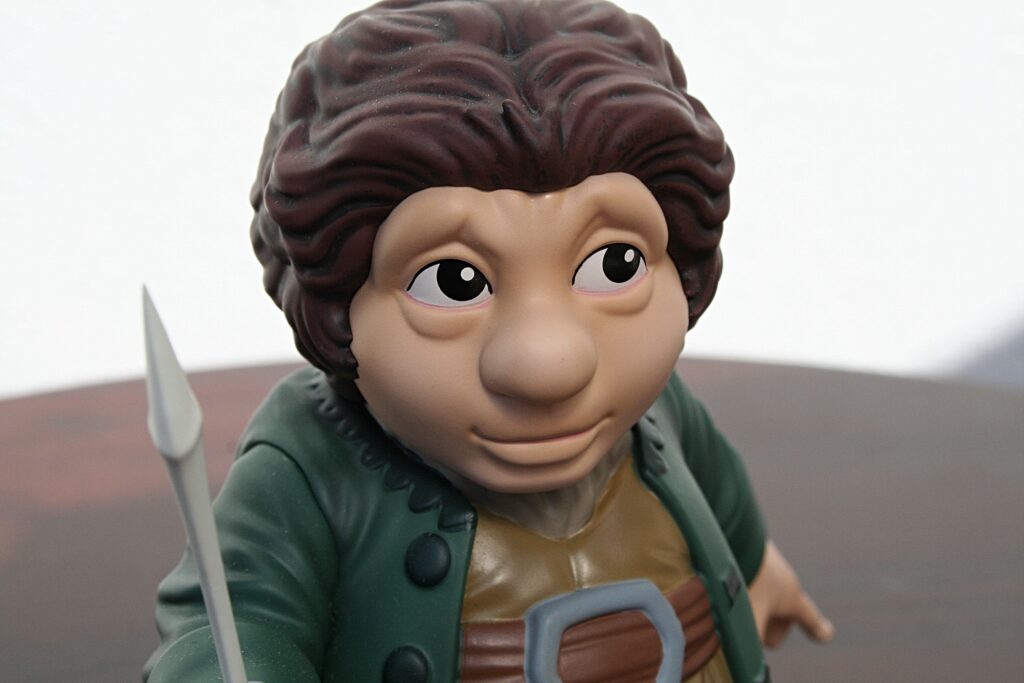 Close-up of a cartoon boy figurine with brown hair, wearing a green coat and holding a sword.