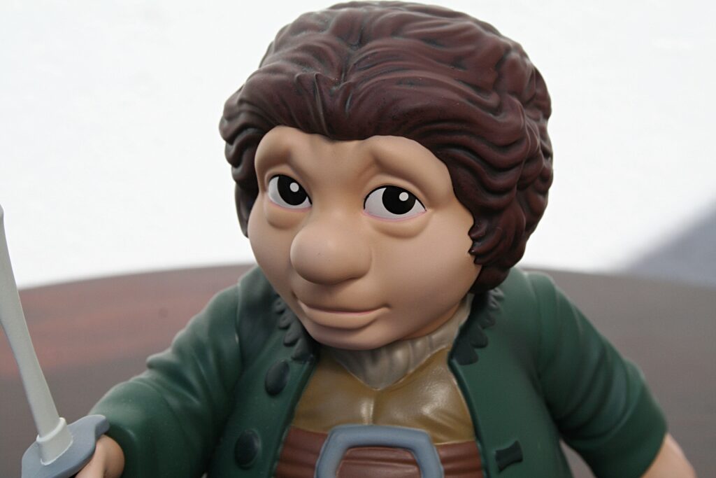 Close-up of a toy figure's face with brown curly hair, wearing a green outfit and holding a light gray sword hilt in the foreground.