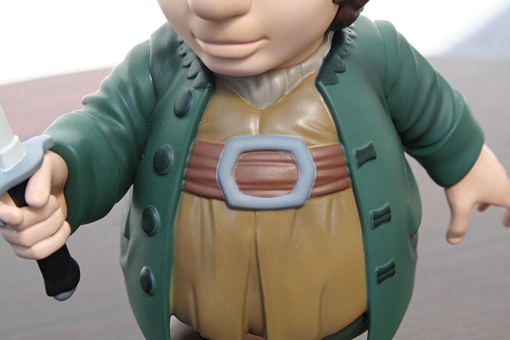 Close-up of a toy figurine's torso: green coat, brown belt, and beige tunic with visible hands at the sides.