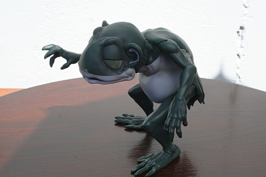 Clay sculpture of a dark green amphibian-like creature reaching forward on a wooden table.