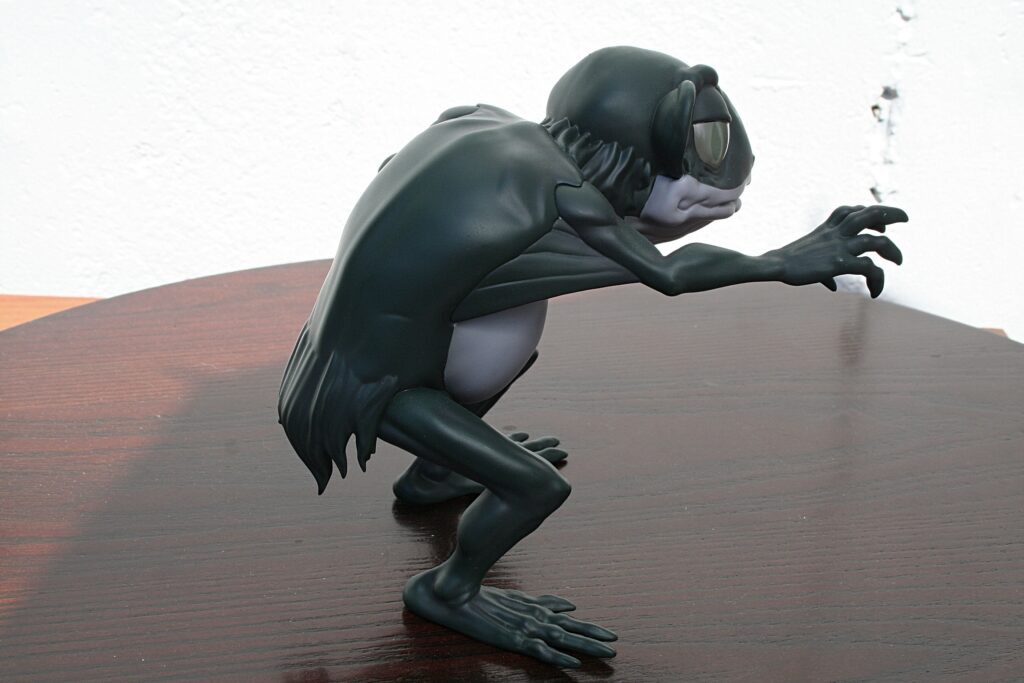 Dark humanoid sculpture crouching on a wooden table, reaching forward with elongated fingers.