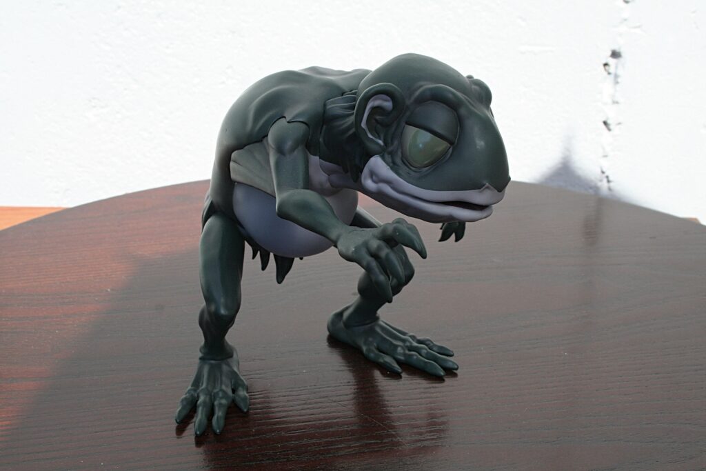 Dark green frog‑like sculpture crouches on a polished wooden table, close view from the side