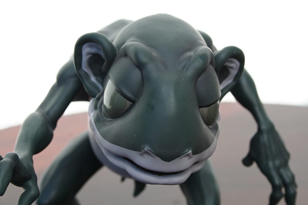 Close-up of a dark gray clay sculpture resembling an alien insect with curved limbs on a flat surface.