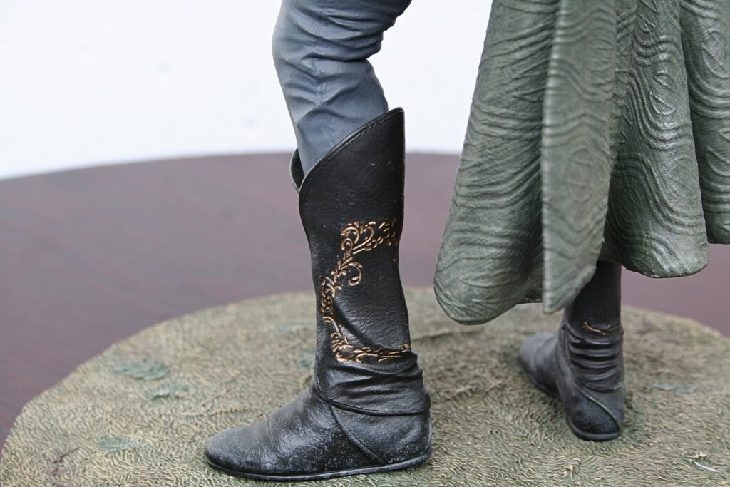 Close-up of black boots with decorative gold pattern on a statue's feet standing on a textured base.