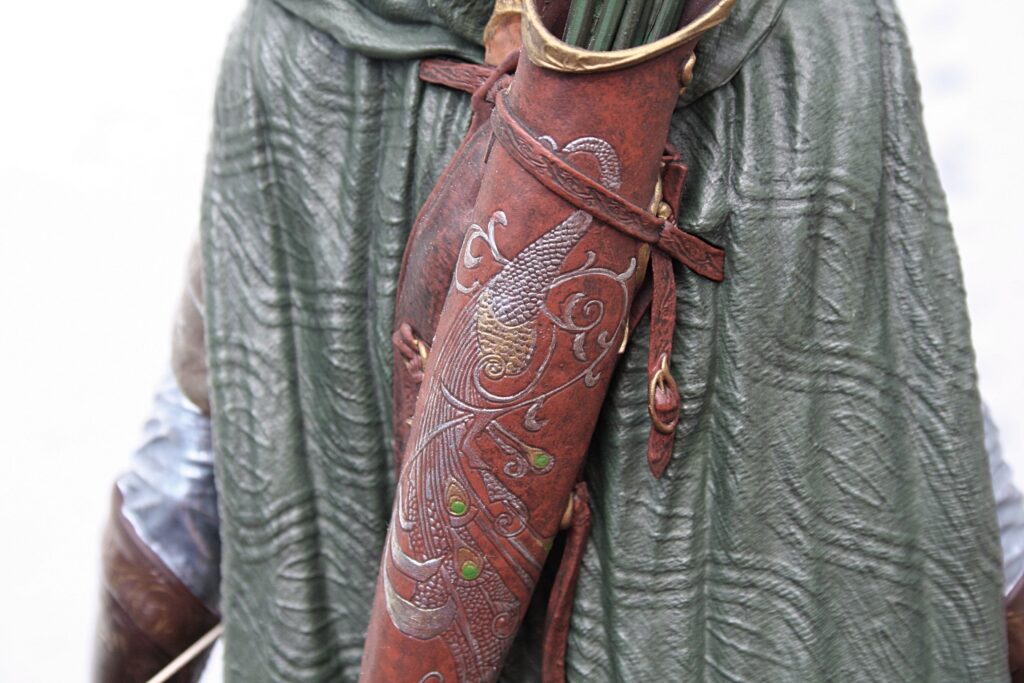 Person in a green textured cloak wearing a red dragon-engraved leather sword scabbard.