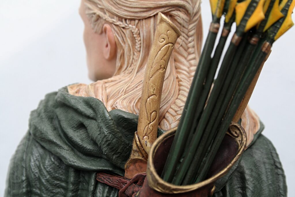 Back view of a carved figurine with braided hair, wearing a green cloak and carrying a quiver of arrows.