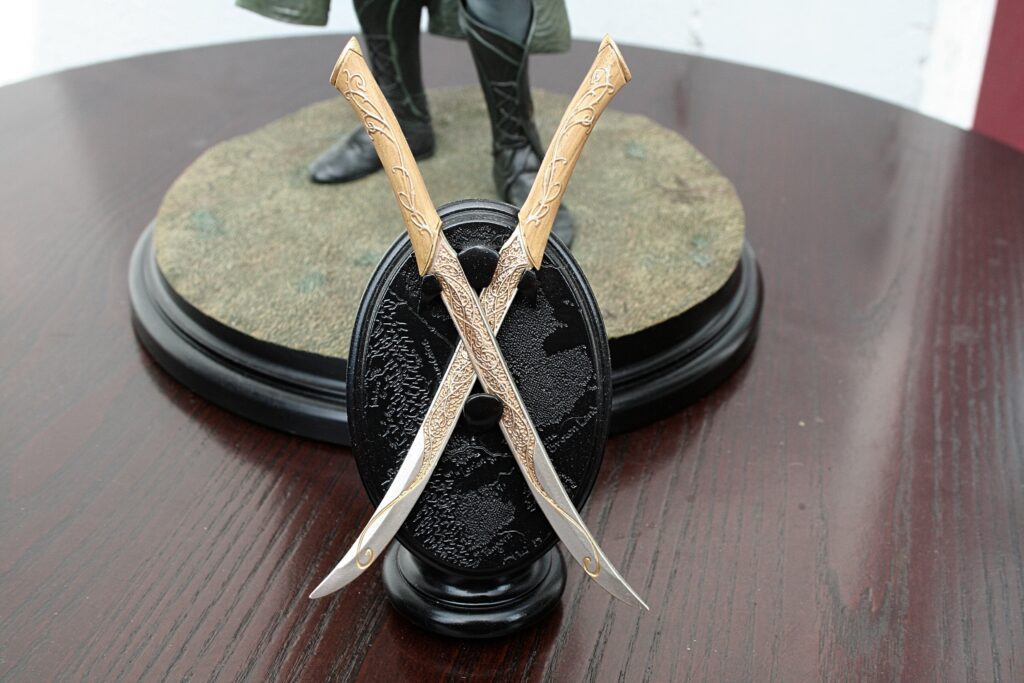 Two ornate golden blades crossed over a glossy black base on a wooden surface, part of a display piece.