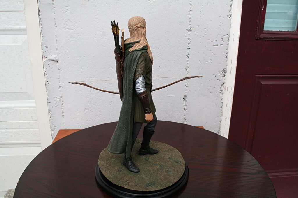 Rear view of a fantasy elf archer figurine with a quiver of arrows on its back and a bow, wearing a green cloak, on a circular base to a tabletop display.