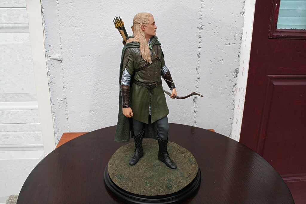 3D model of Legolas-like elf archer figure standing on a round display base with a quiver of arrows on his back and a bow at his side, indoors against a textured wall backdrop.