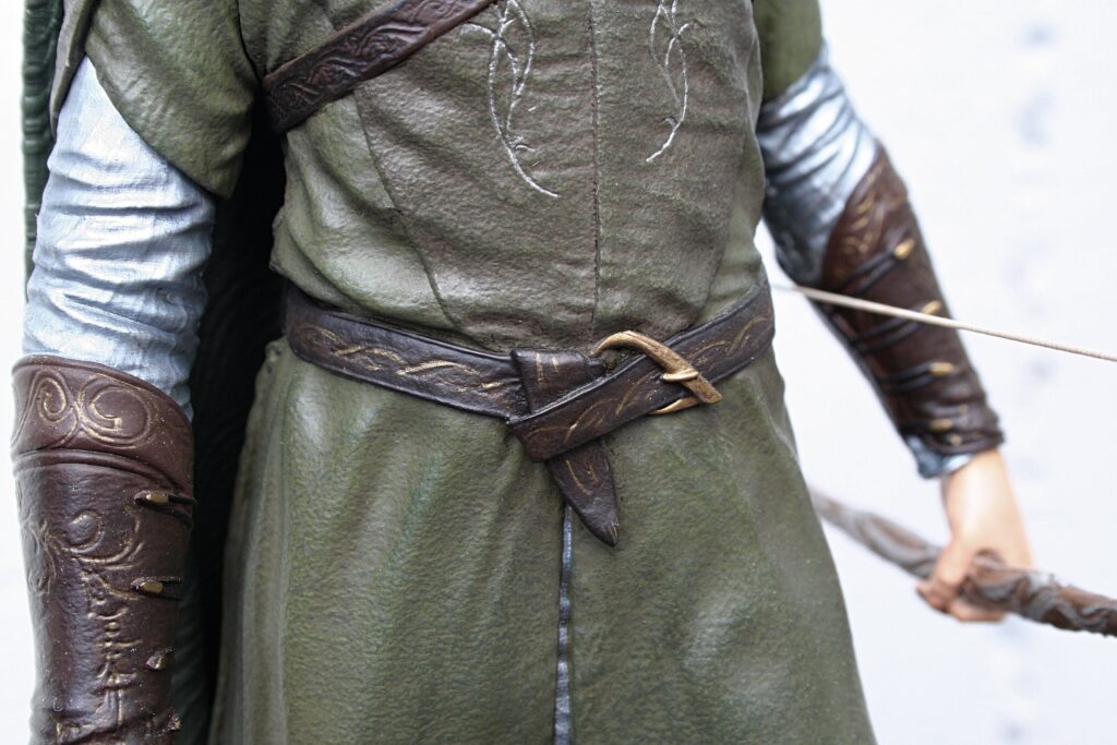 Close-up of a costumed figure wearing a green leather tunic with a braided brown belt and ornate brown bracers.