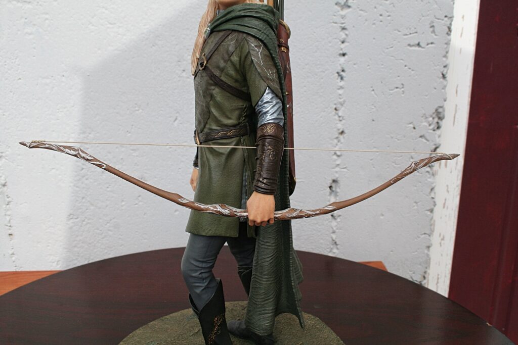 Person in medieval costume stands sideways, holding a decorative longbow with carved details.