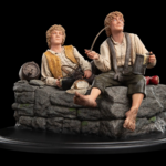 Two carved figurines of rustic men sitting on a stone wall, one pouring from a jug while the other holds a bowl and pipe.