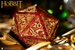 Close-up of a glittery red and gold D20 dice ornament with ornate patterns, The Hobbit logo visible in the corner.