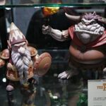 Two The Hobbit figurines in a glass display: a bearded dwarf with sword and shield on the left, and a horned, tusked creature in a red cloak on the right.