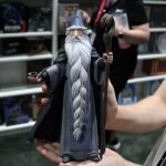 Small wizard figurine with blue hat and long white beard being held in both hands, indoors in a store.