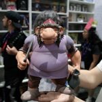 A large purple troll figure being held up by a person, with swords in its hands, in a toy store display background.