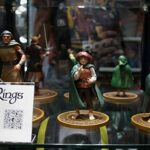 Lord of the Rings action figures on a display shelf in a storefront window, with a sign and QR code visible in the foreground.