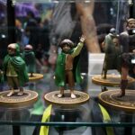 Three small fantasy figurines in green cloaks on circular bases inside a glass display case.