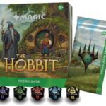 Boxed Magic: The Gathering prerelease kit themed around The Hobbit with a hobbit, wizard, and round door artwork; includes five black and colored dice and a card sleeve.