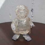 Transparent crystal figurine of a person in a spacesuit holding a small blade, placed on a dark wooden table.