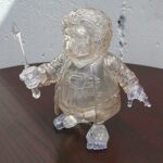 Crystal glass figurine of a knight in armor kneeling on a dark table, holding a blade in its right hand.