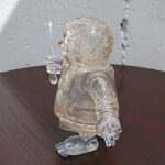 Crystal glass bust of a person holding a dagger upright beside their head on a dark wooden table