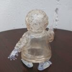 Clear glass baby figurine with textured hair and outstretched arms sitting on a dark wooden table