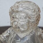 Close-up of a transparent glass bust sculpture with swirling textures and reflections on the head and shoulders.