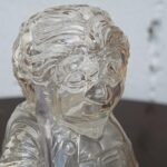 Close-up of a clear glass bust depicting a child in a suit, with swirling internal patterns and reflections coolly refracting light.