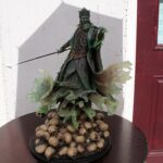 Green-caped king statue with crown and sword, standing atop a pedestal surrounded by small skulls on a round table.