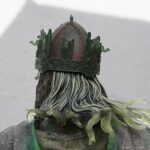 Close-up of a statue's ornate crown with a green patina, viewed from the back with flowing hair underneath.