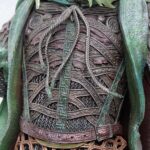 Close-up of ornate leather chest armor with braided cords and green fabric ribbons on a fantasy costume.