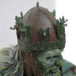 Close-up of a statue head wearing an ornate crown with green patina and intricate carvings in the metalwork.