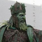 Statue of a bearded king in ornate green armor with a detailed crown and flowing beard