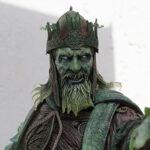 Bronze-green statue of a crowned king in ornate armor with a beard, facing forward.