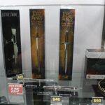 Display case with boxed sword replicas, including The Lord of the Rings and Star Trek items, with price tags visible